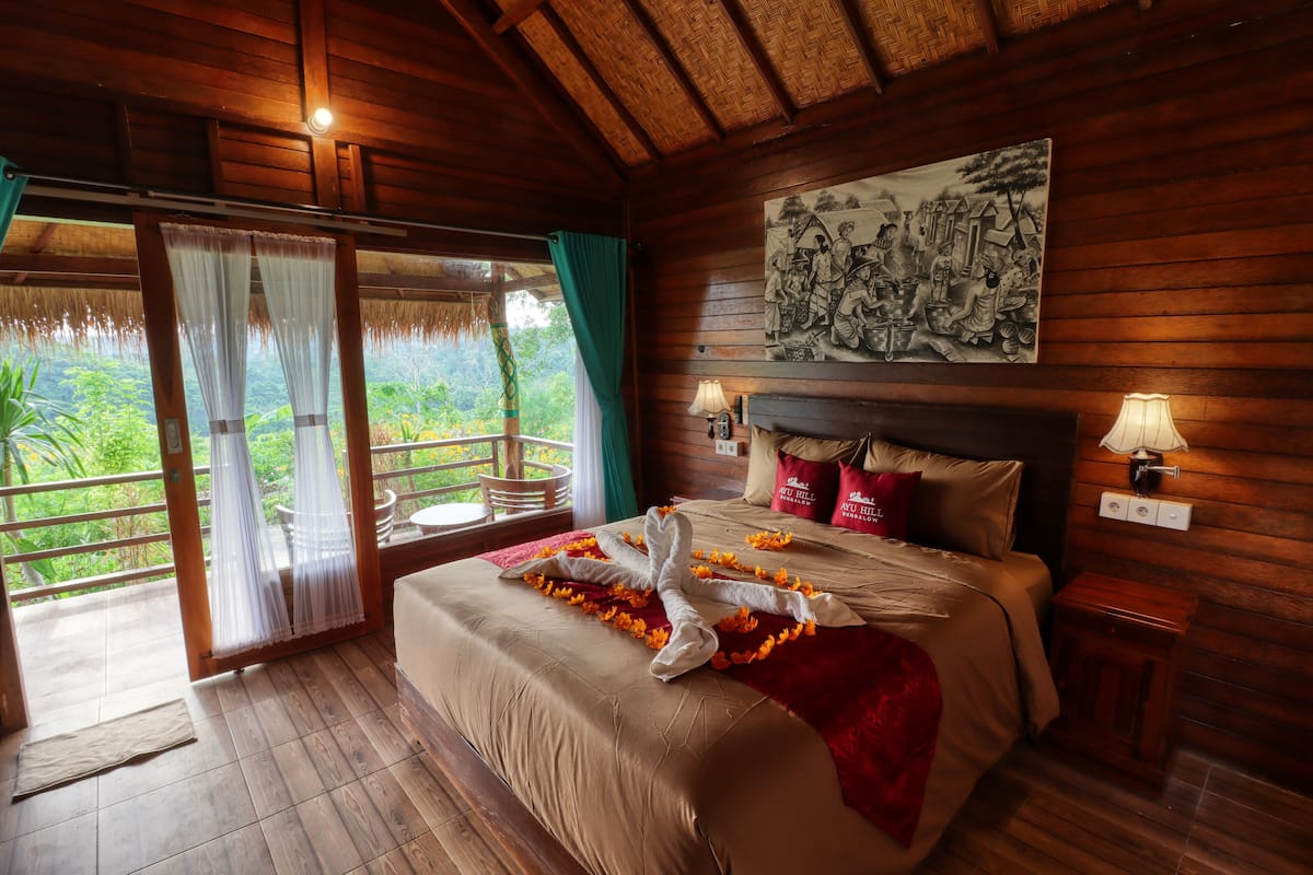 Een houten kamer met een bed, een schilderij en een balkon met uitzicht op groen.