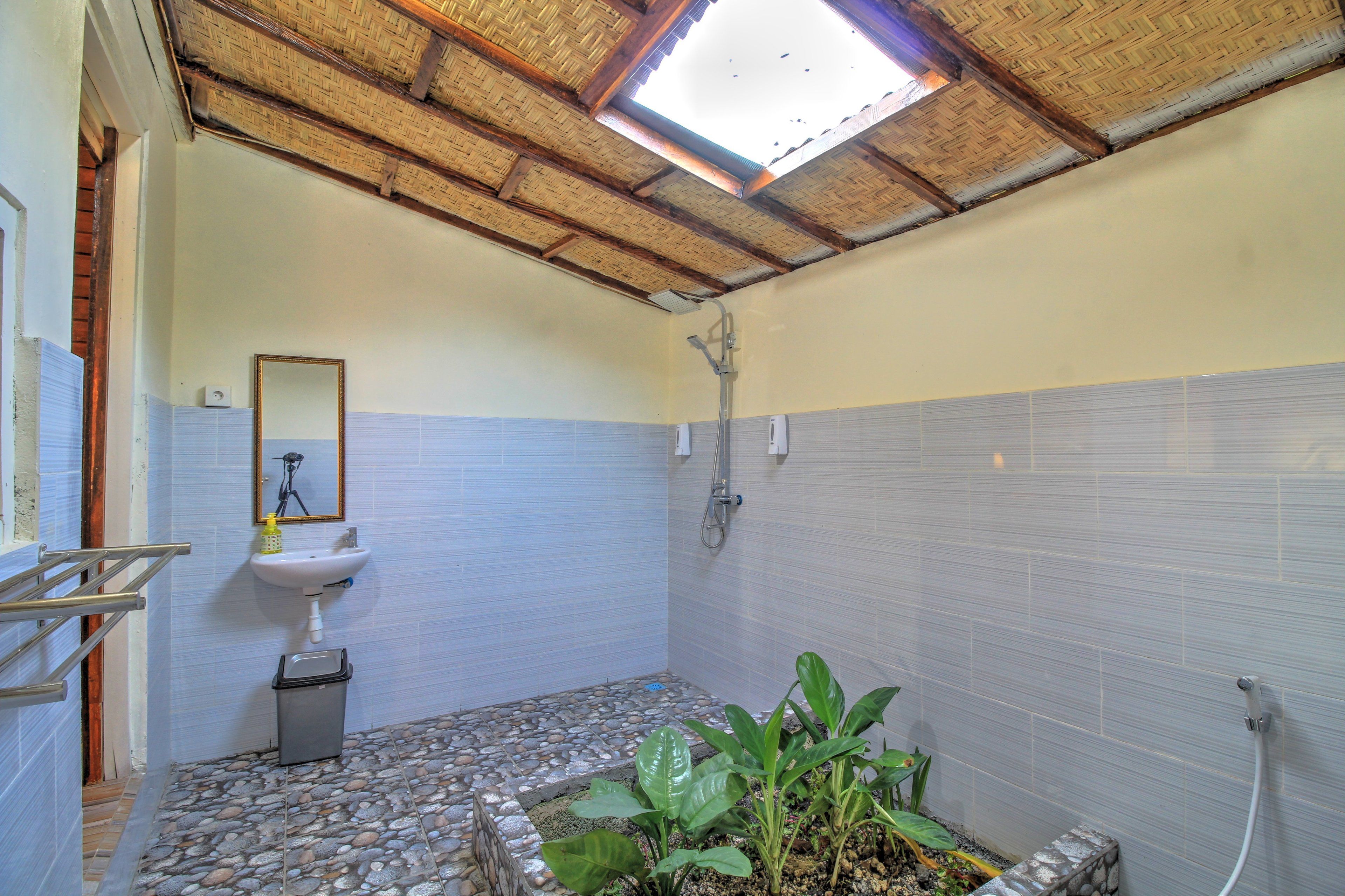 A bathroom with a stone-tiled floor, a white sink, a mirror, and a shower.