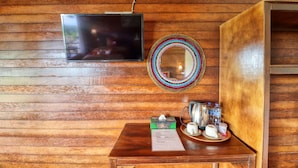 Een houten wand met een flatscreen televisie, een kleurrijk spiegelbeeld, en een tafel met zakdoosjes, theepot, kopjes en een menukaart.