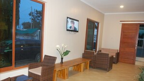 Una habitación con muebles de mimbre, un banco de madera y un televisor en la pared.