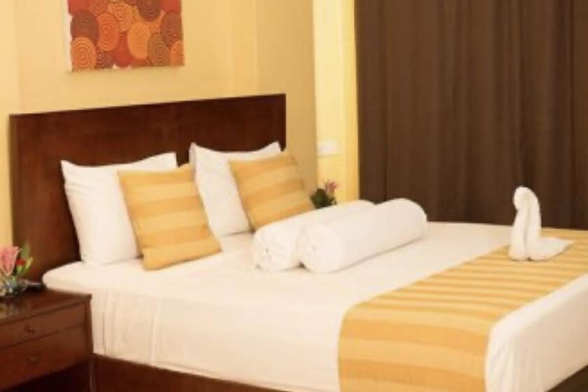 Una cama bien hecha con ropa blanca y a rayas, un cabecero de madera y una mesita de noche con una lámpara.