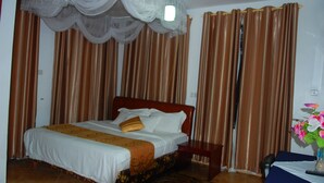 Una habitación de hotel con cama, cortinas, mesita de noche y un jarrón con flores.