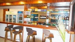Una zona de bar con taburetes, un refrigerador y estantes llenos de botellas.