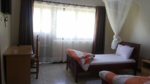 A bedroom with a bed, a desk, and a chair. - Hotel Premier (Yumbe)