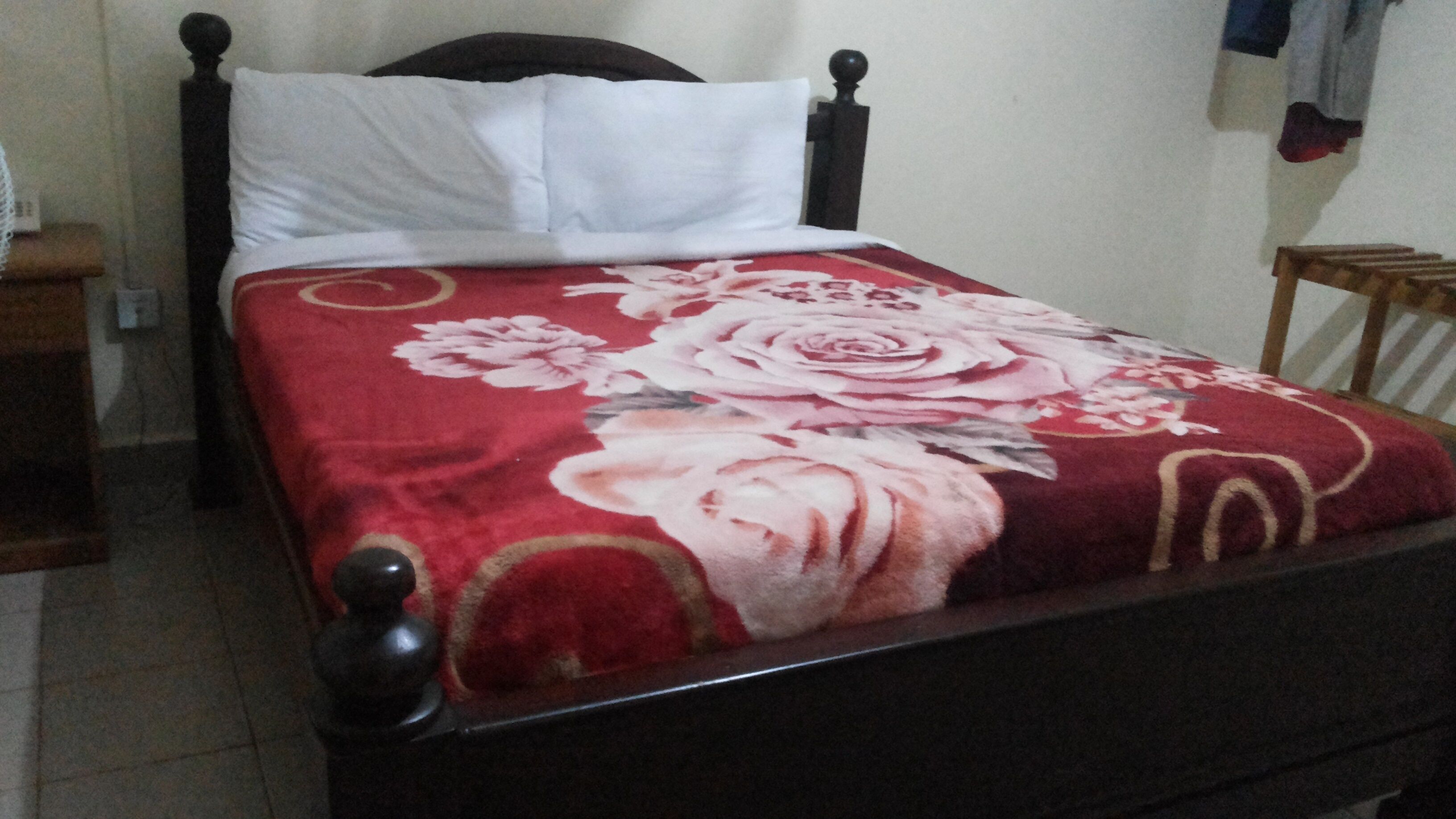A bed with a floral bedspread, a wooden headboard, and a white pillow.