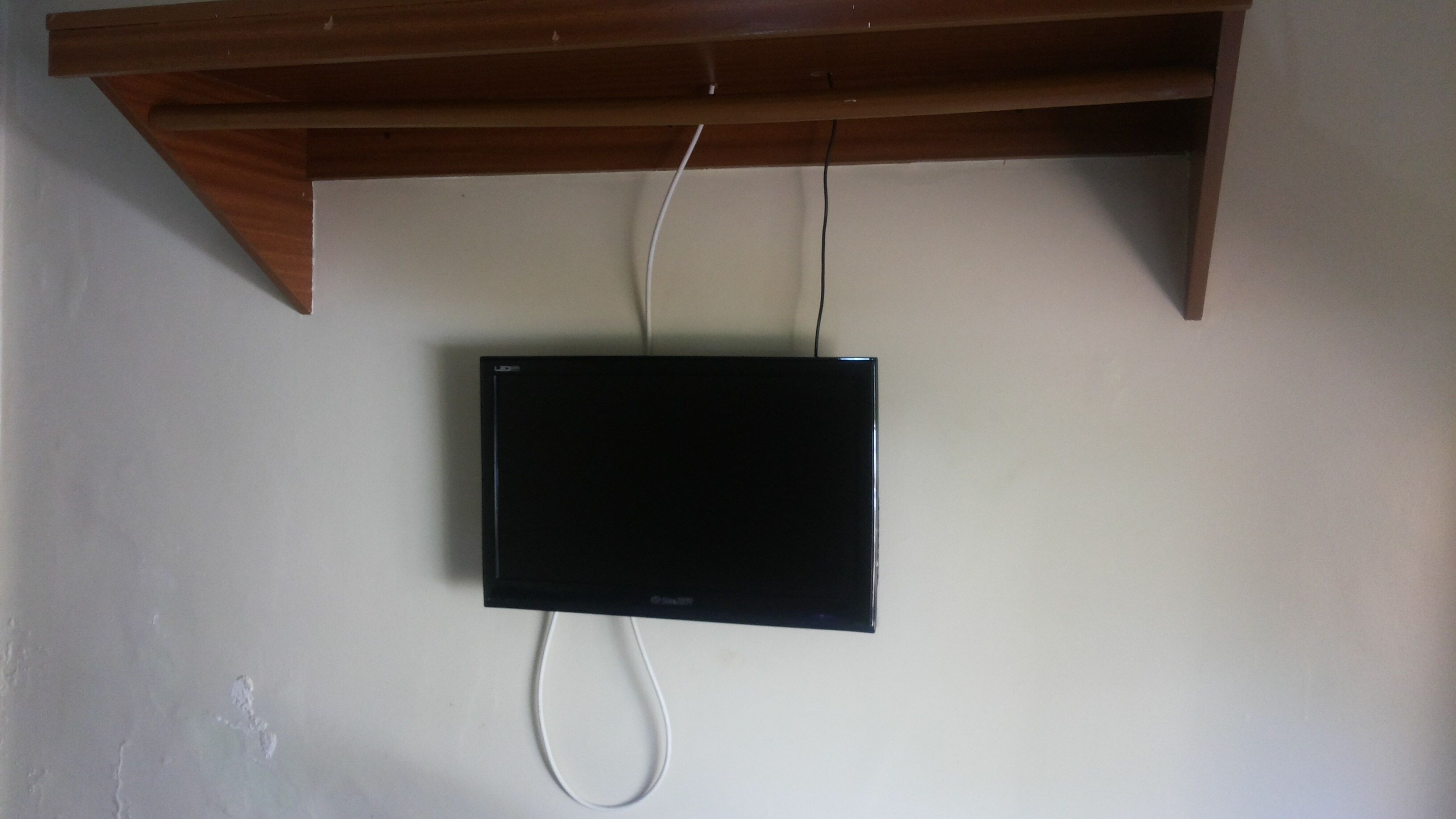 Een zwarte flatscreen-tv bevestigd aan een muur, met een houten plank erboven.