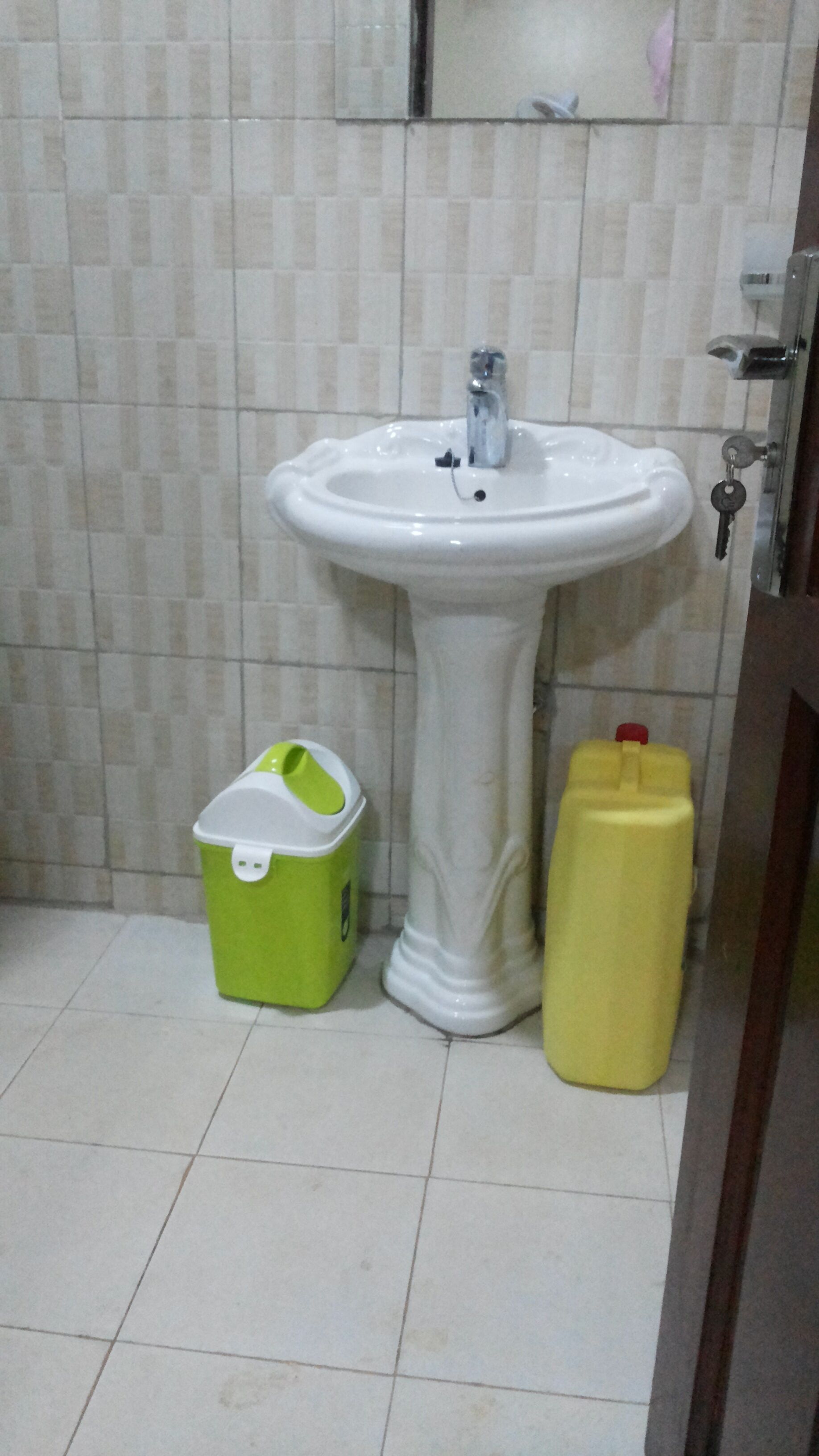 A bathroom with a white pedestal sink, a green trash bin, and a yellow water jug.