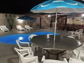 An outdoor pool area with lounge chairs, a table, and umbrellas.