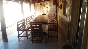 Una taula de fusta llarga amb seients, situada en una habitació amb sòls de rajola i una paret de pedra decorada amb plantes i elements penjants.