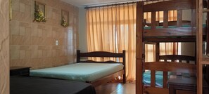 Quarto com cama, uma cadeira de madeira, uma mesa pequena, interruptor de luz na parede e janela com cortinas.