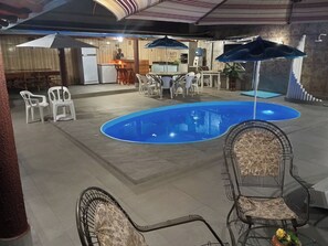 An indoor swimming pool with lounge chairs and umbrellas, surrounded by a dining area with tables and chairs. - HIGH SOBRADO STANDARD SEASON IN NEW CALDAS (CALDAS NOVAS)