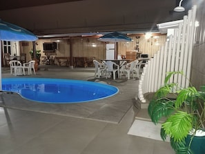 An indoor pool area with a blue pool, surrounded by white plastic chairs and tables, and a potted plant. - HIGH SOBRADO STANDARD SEASON IN NEW CALDAS (CALDAS NOVAS)