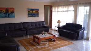 Un saló amb un sofà de cuir fosc, una taula de centre de fusta i una làmpada sobre una taula auxiliar. Hi ha dos quadres penjats a la paret.