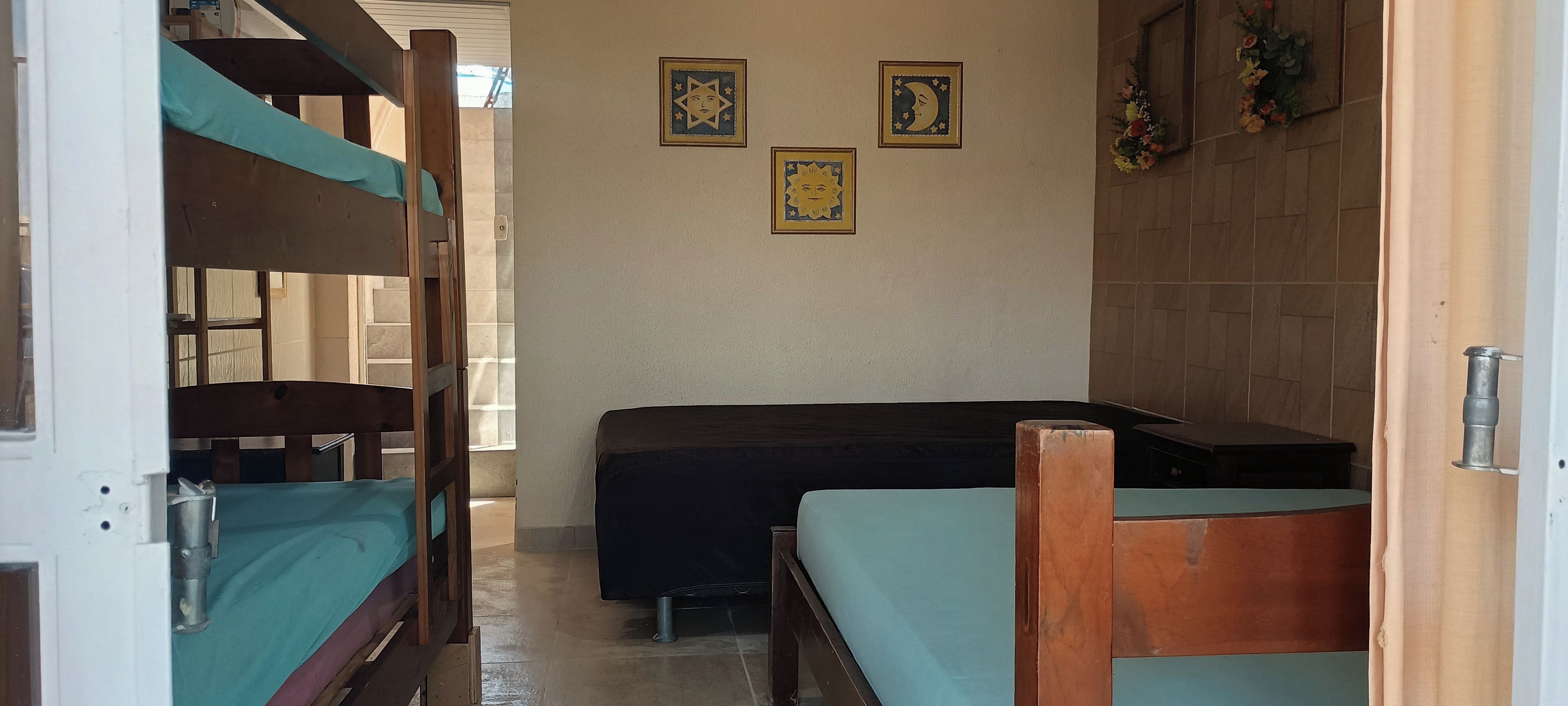 A room with bunk beds, a single bed, and a small table. There are three framed pictures on the wall.