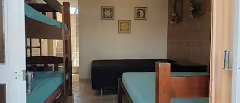 Una habitación con literas, una cama individual y una mesita pequeña. Hay tres cuadros enmarcados en la pared.