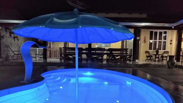 Una piscina amb un ombrell amb llums blaves, taules i cadires al fons.