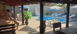A covered outdoor area with a pool, lounge chairs, and a dining setup.