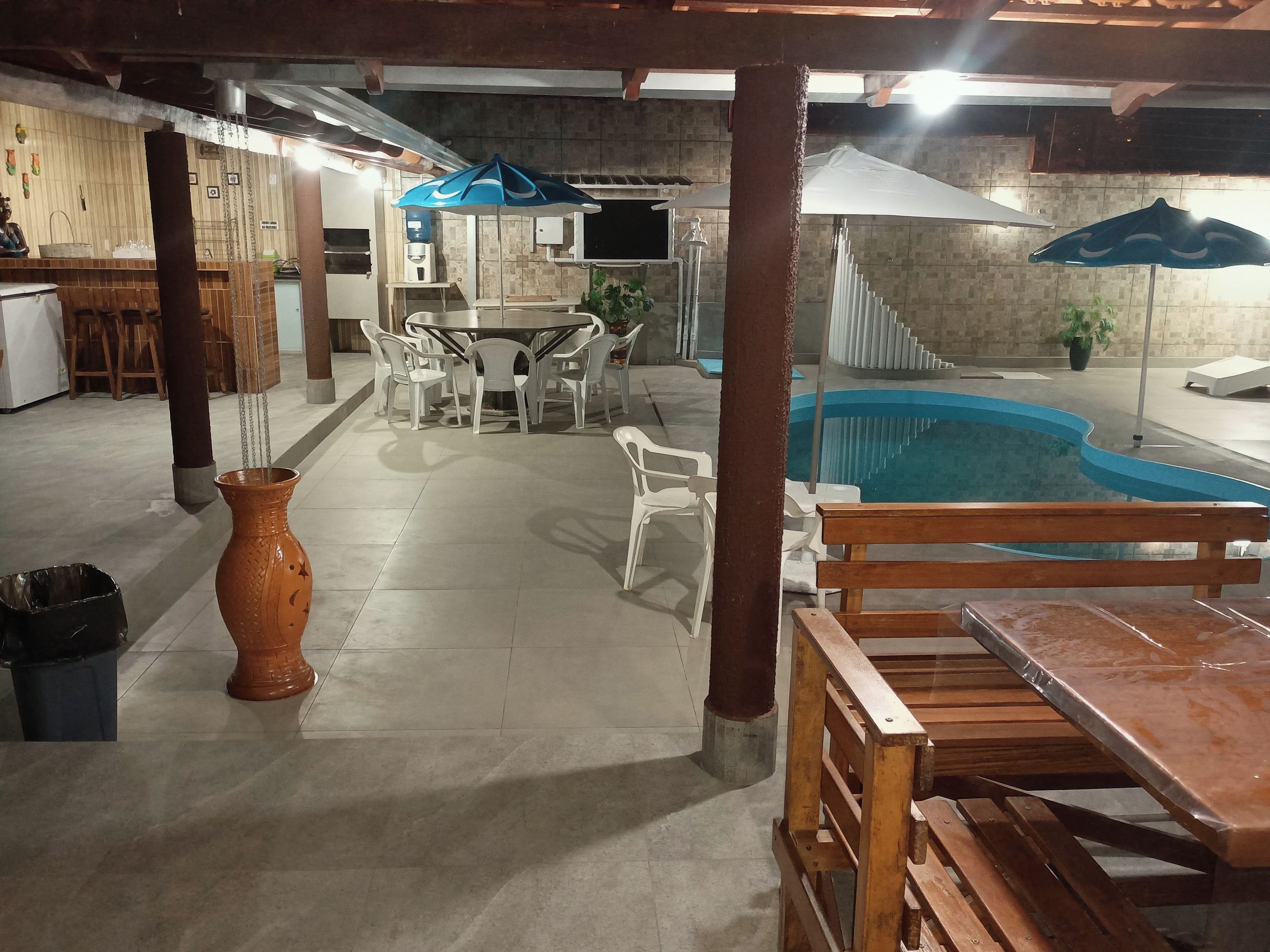 An indoor pool area with a table and chairs, a wooden bench, and a trash bin.