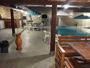 An indoor pool area with a table and chairs, a wooden bench, and a trash bin. - HIGH SOBRADO STANDARD SEASON IN NEW CALDAS (CALDAS NOVAS)