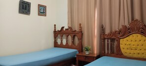 A room with two beds, a wooden headboard with a yellow tufted section, and a small table with a plant.
