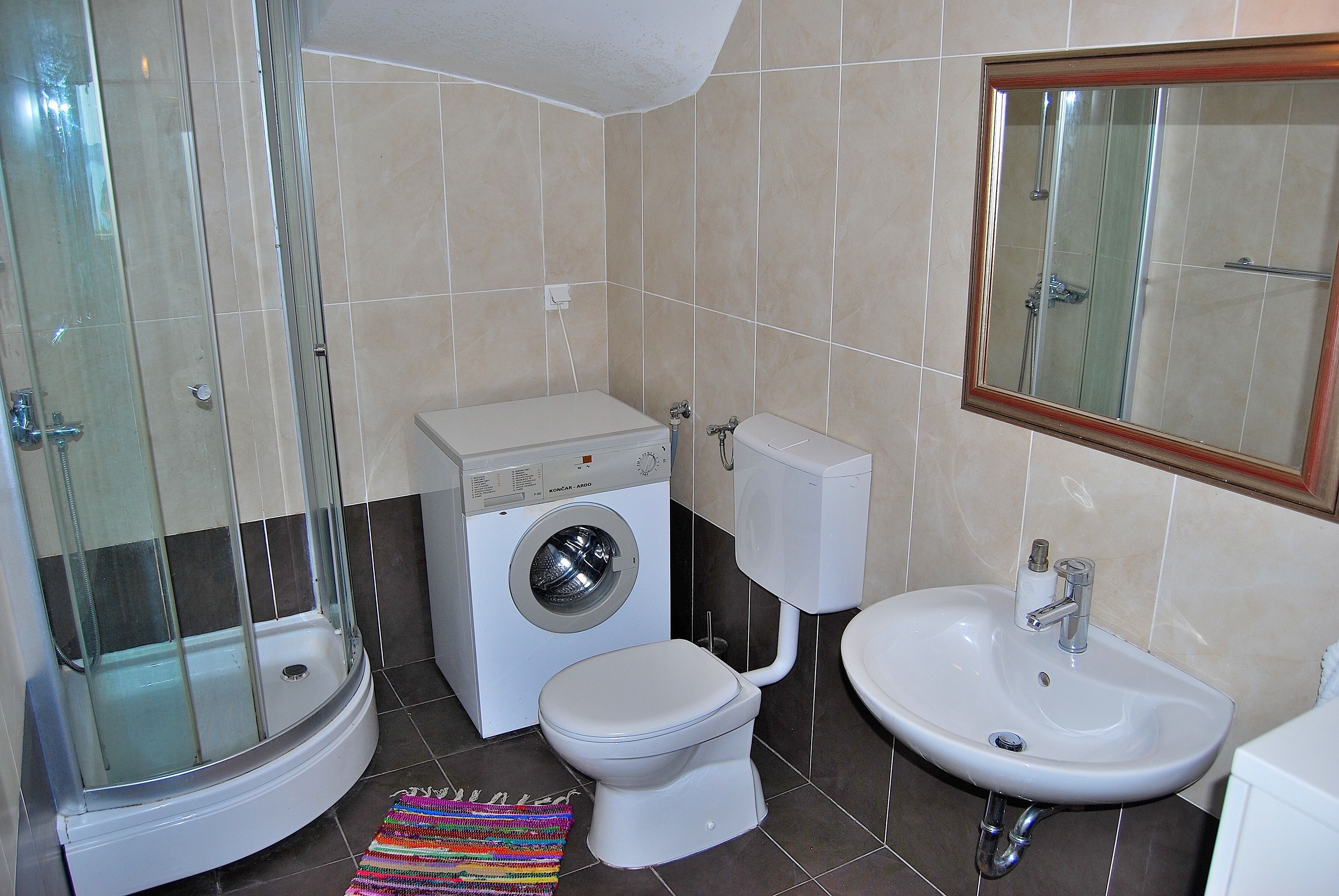 Une salle de bain compacte avec une douche à parois de verre, un lave-linge, des toilettes et un lavabo.