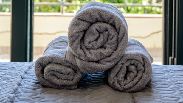 A bed with rolled towels and a view of a balcony with greenery and mountains in the background. - Elies Villa (Kalymnos)