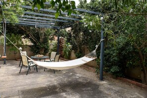 A hammock suspended between two poles in a garden area with a table and chairs underneath.
