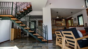 A spacious living area with a wooden staircase, a dining table with chairs, and a kitchen in the background. - Elies Villa (Kalymnos)