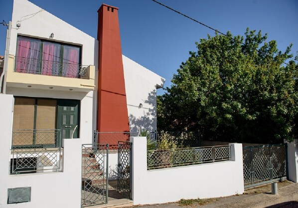 A modern two-story building with a red chimney, a balcony with a metal railing, and a gated entrance.