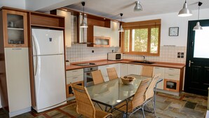A modern kitchen with a glass dining table, wicker chairs, a refrigerator, a microwave, and a sink. - Elies Villa (Kalymnos)