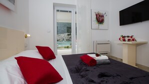 Une chambre d’hôtel moderne équipée d’un lit, d’une télévision, d’une fenêtre donnant sur la mer et d’un petit bureau agrémenté d’une plante.