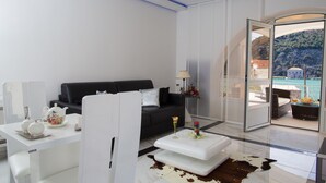 Un salon moderne avec un canapé noir, une table basse blanche et une porte vitrée donnant sur un balcon d’où l’on peut admirer une montagne et une piscine.