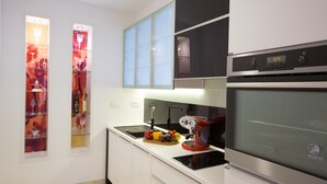 Une cuisine moderne avec des meubles blancs, un four noir et une machine à café rouge.