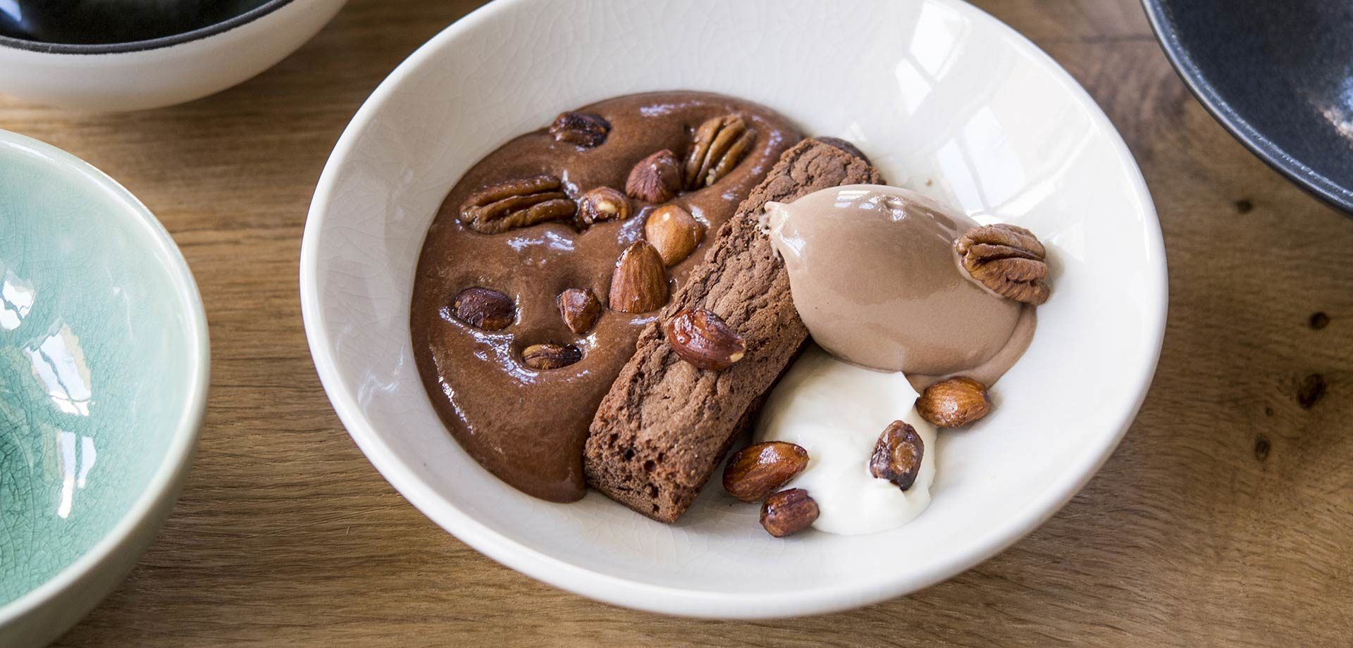 Een nagerechtbord met chocolademousse, koekjes en noten op een houten tafel.