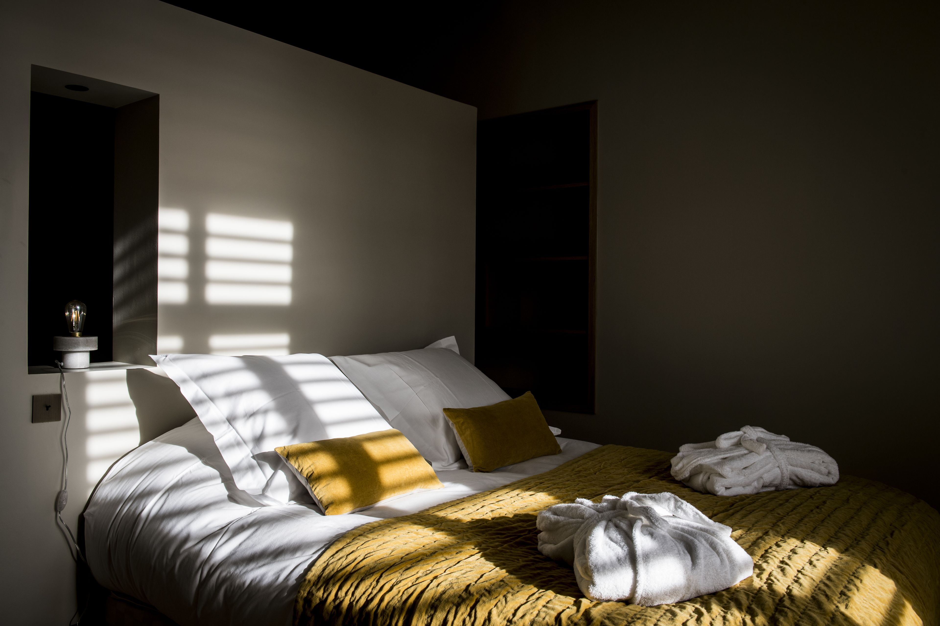 Una cama bien hecha con sábanas blancas, un plaid amarillo y un par de toallas blancas.