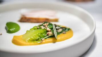 A plate with a dish of greens, nuts, and a yellow sauce, and a slice of meat on a white plate.