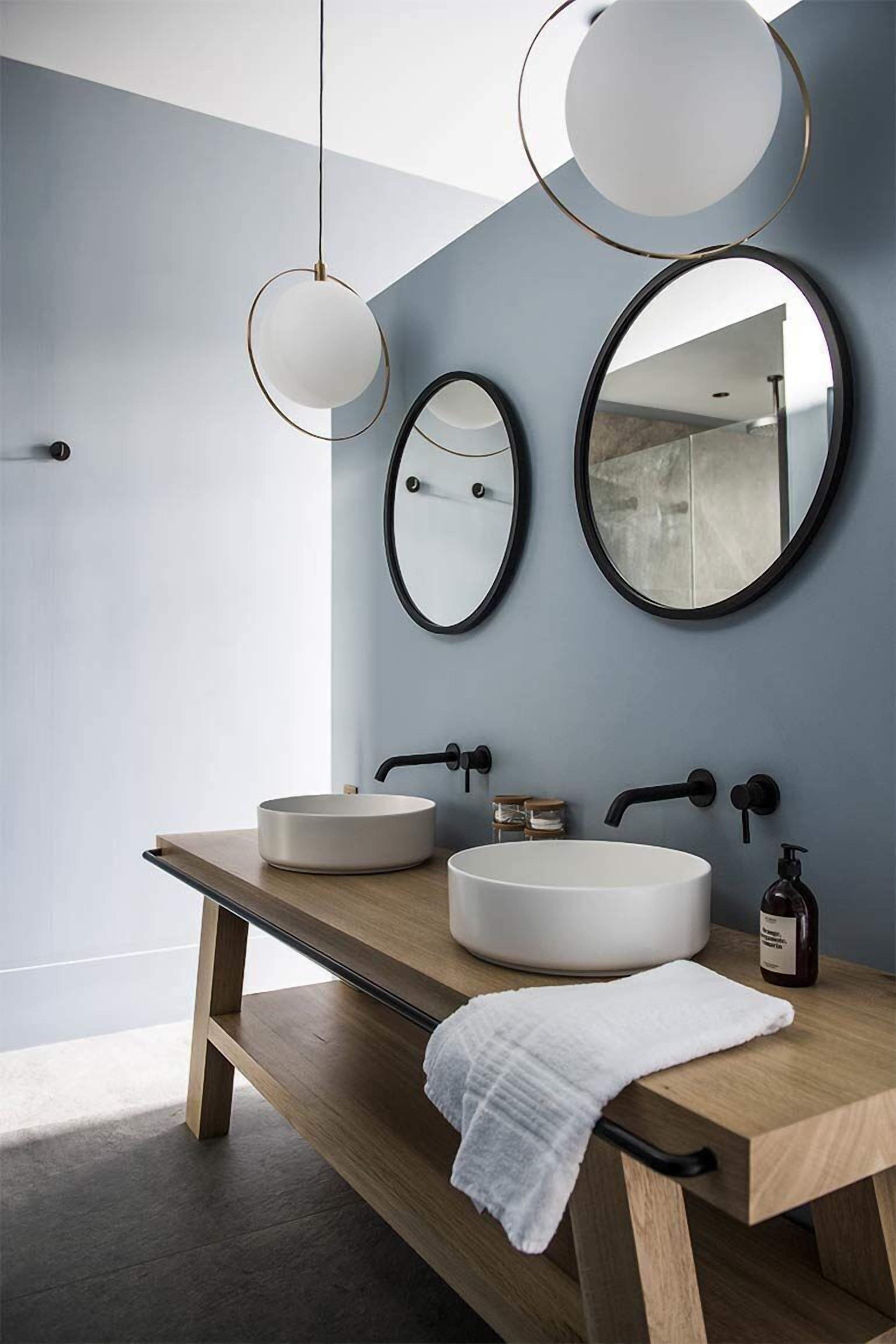 Un baño moderno con dos espejos redondos, un mueble de tocador de madera y un lavabo blanco.