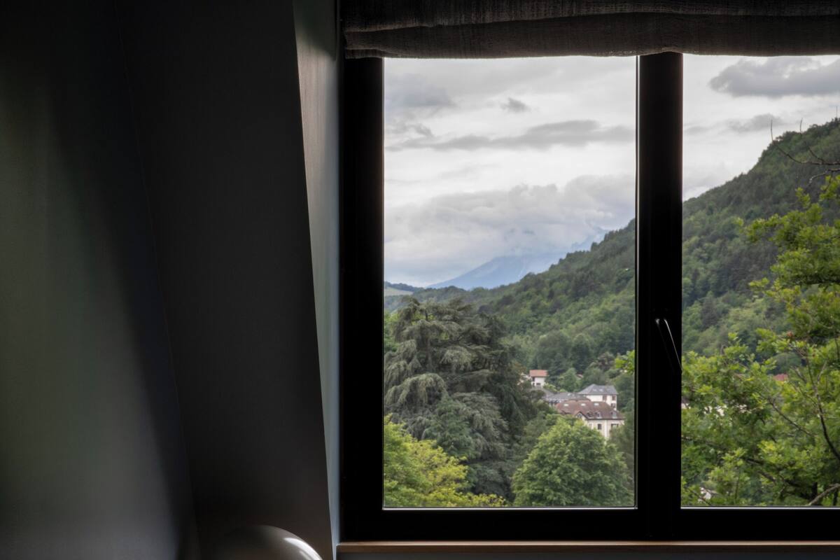 Una habitación con escritorio, silla y ventana con vistas a un paisaje montañoso.
