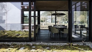 A modern dining area with a glass wall, wooden ceiling, and outdoor seating visible through the glass. - Maison Aribert (Saint-Martin-d'Uriage)