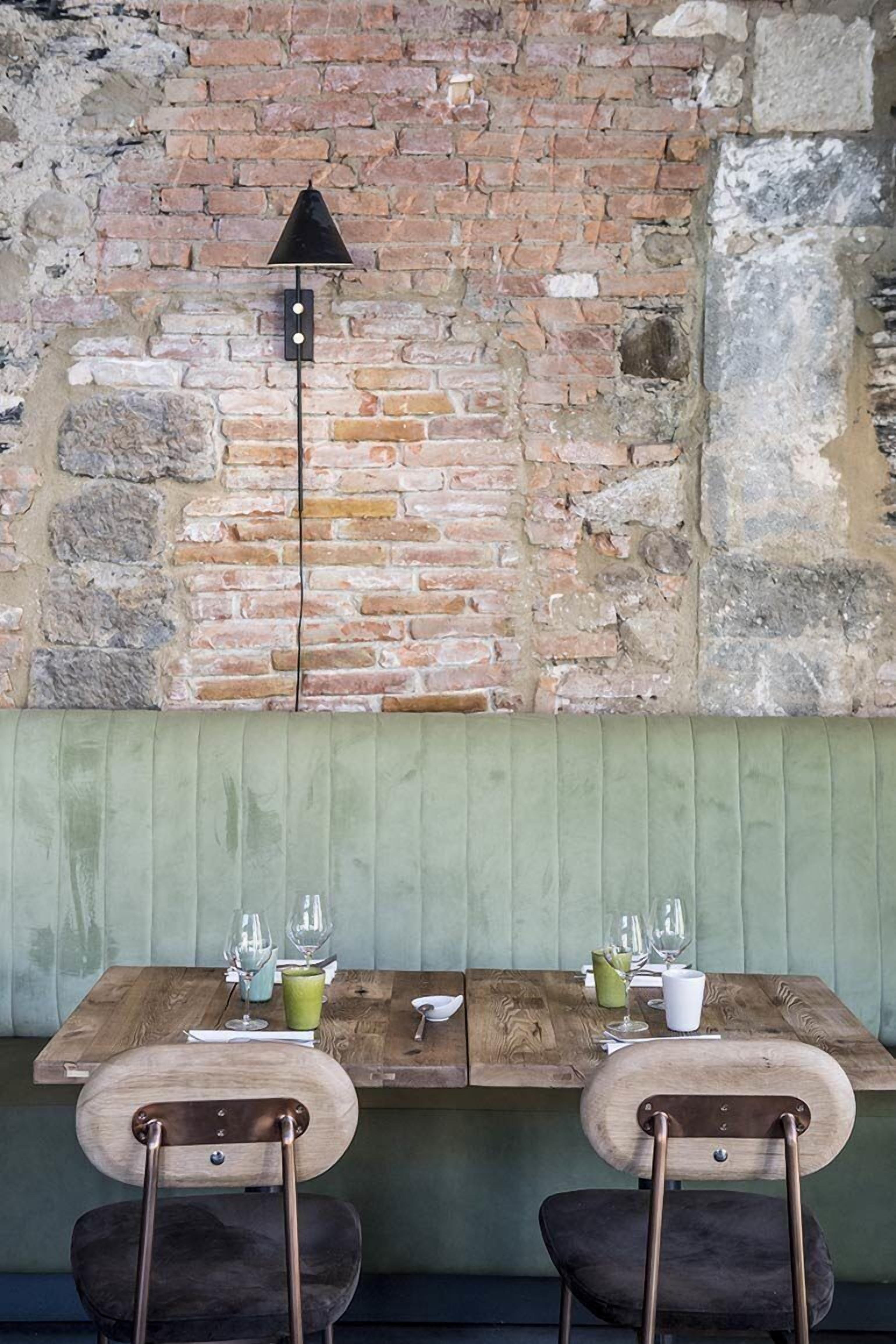 A wooden table with two chairs, a brick wall, and a green cushioned bench.