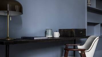 Un escritorio con lámpara, una silla y una estantería frente a una pared azul.