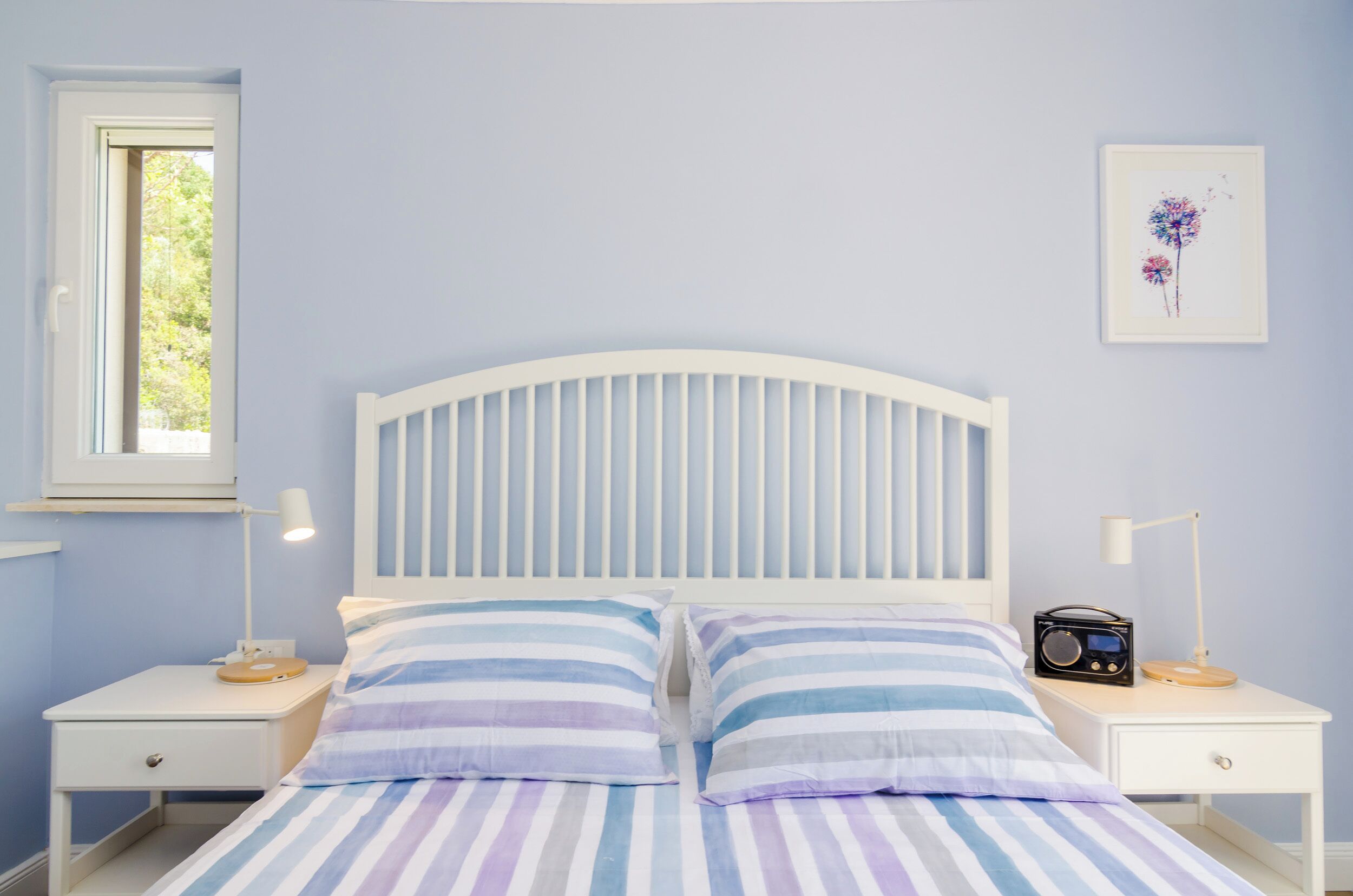 Een slaapkamer met een bed, twee nachtkastjes, een raam en een aan de muur hangend schilderij.