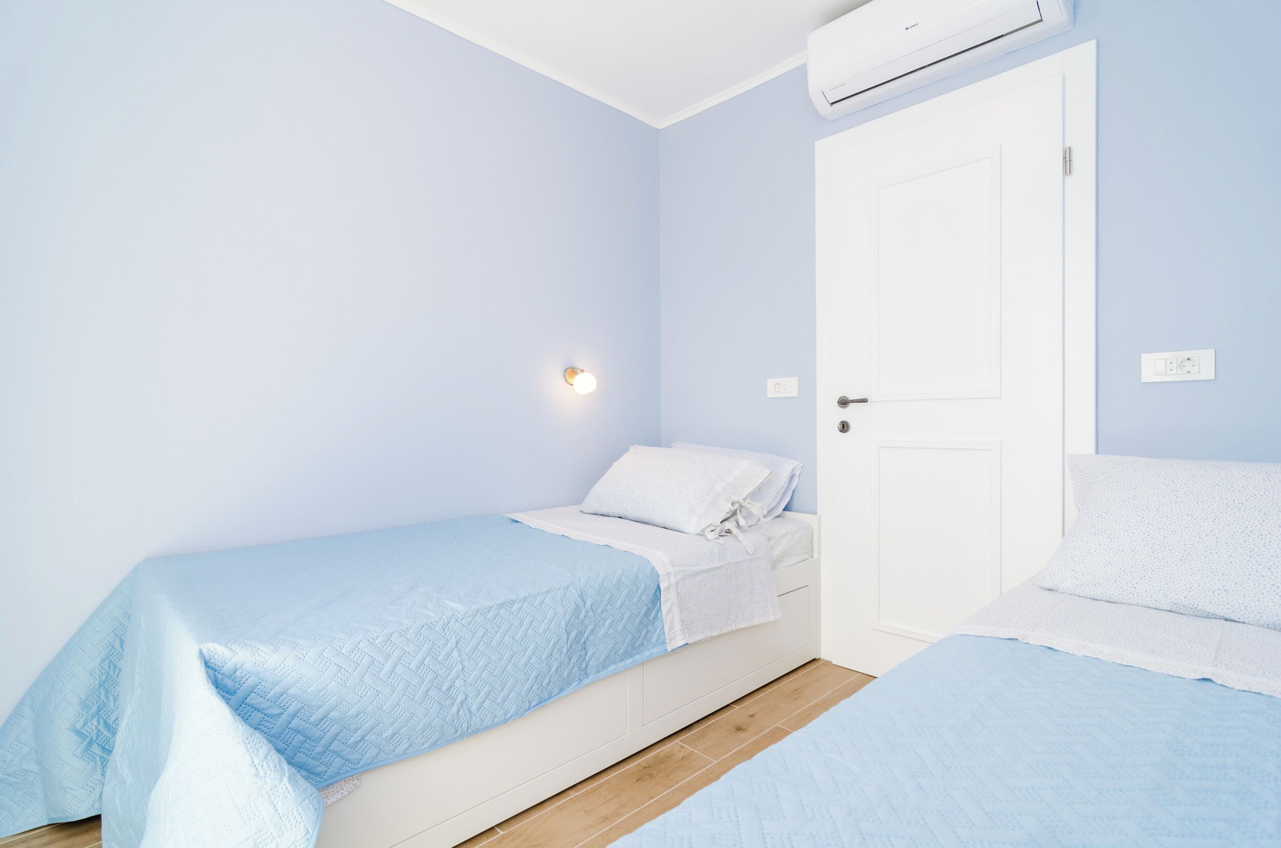 Quarto com duas camas, uma porta branca e um aparelho de ar condicionado.