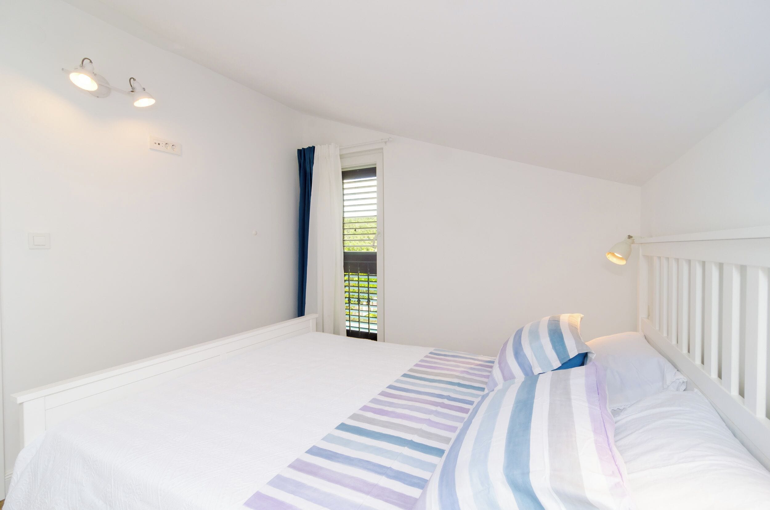 Une chambre à coucher avec un lit, une fenêtre avec des rideaux et un luminaire fixé au mur.