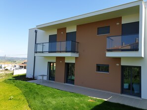 A modern two-story residential building with a flat roof, large windows, and a balcony on the upper floor.