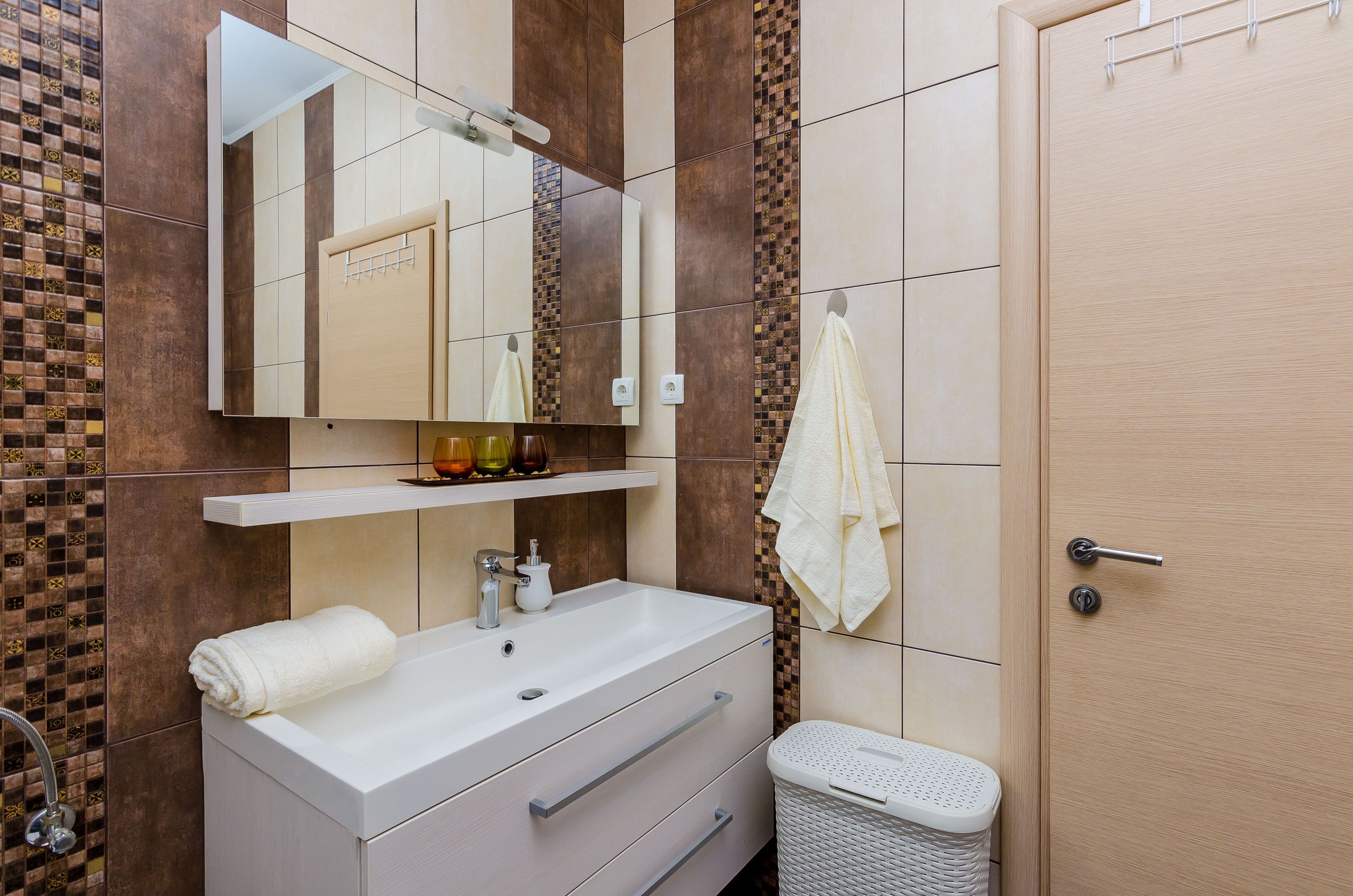 A bathroom with a white sink, mirror, and towel rack. There is a trash bin and a door with a handle.