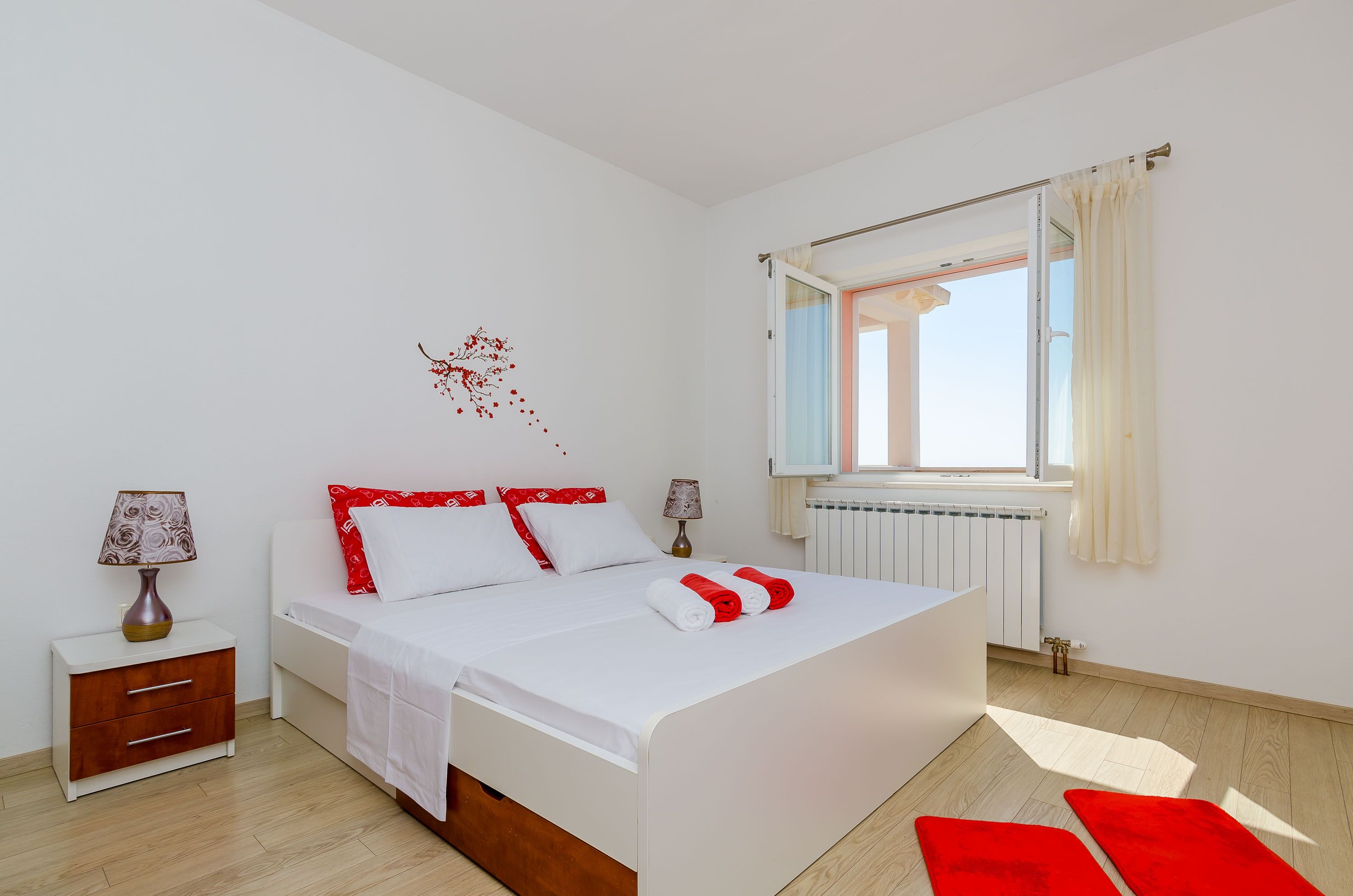 Un dormitori modern amb un llit gran, una tauleta de nit, una làmpada i una finestra amb cortines.