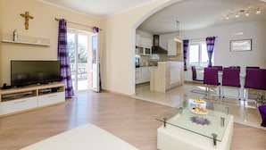 A modern living room with a flat-screen TV, a glass coffee table, and a dining area with purple chairs. - Villa Dragic (Konavle)