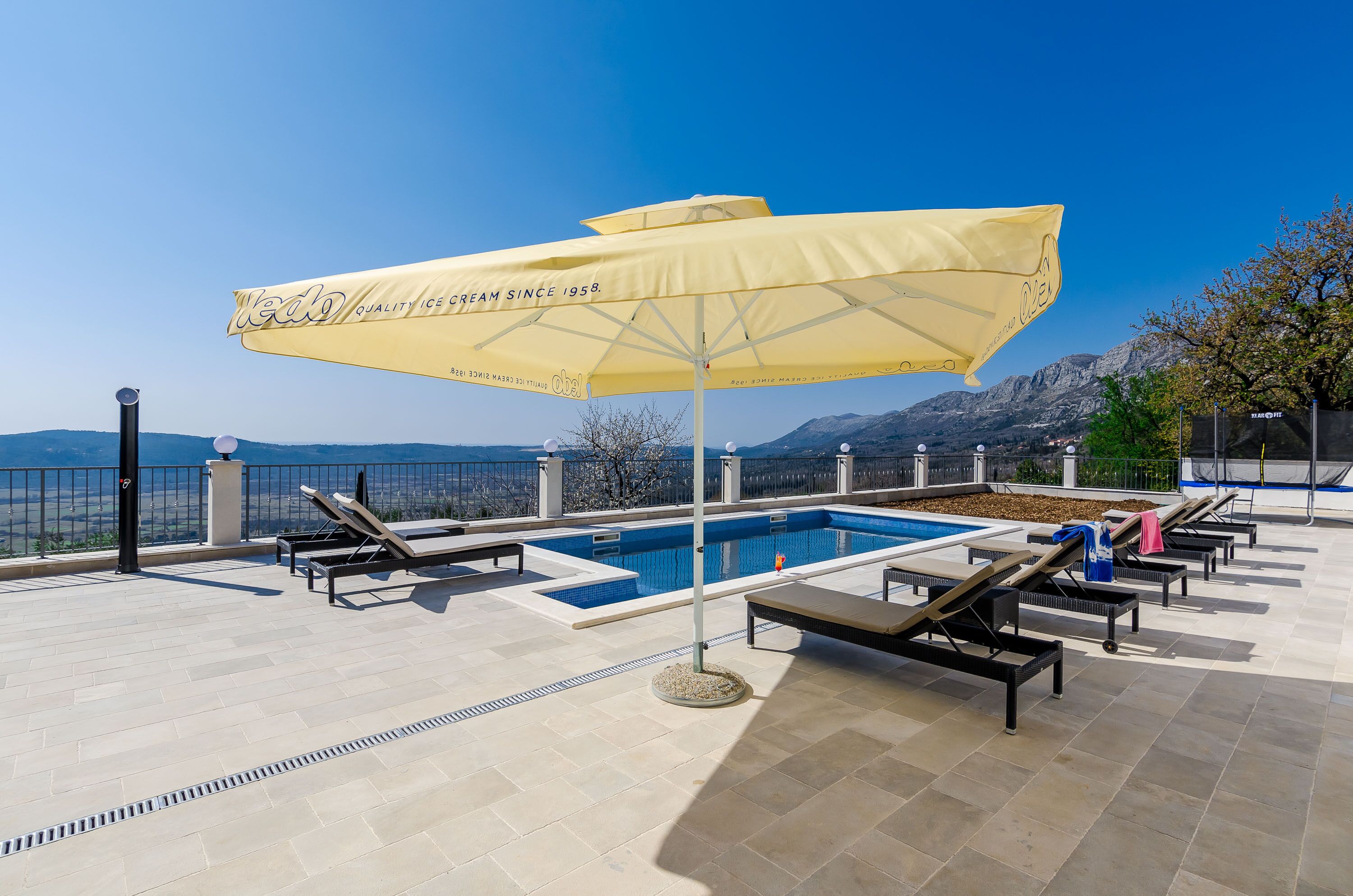 Un espace piscine aménagé sur le toit, avec des chaises longues, une piscine et un parasol jaune.