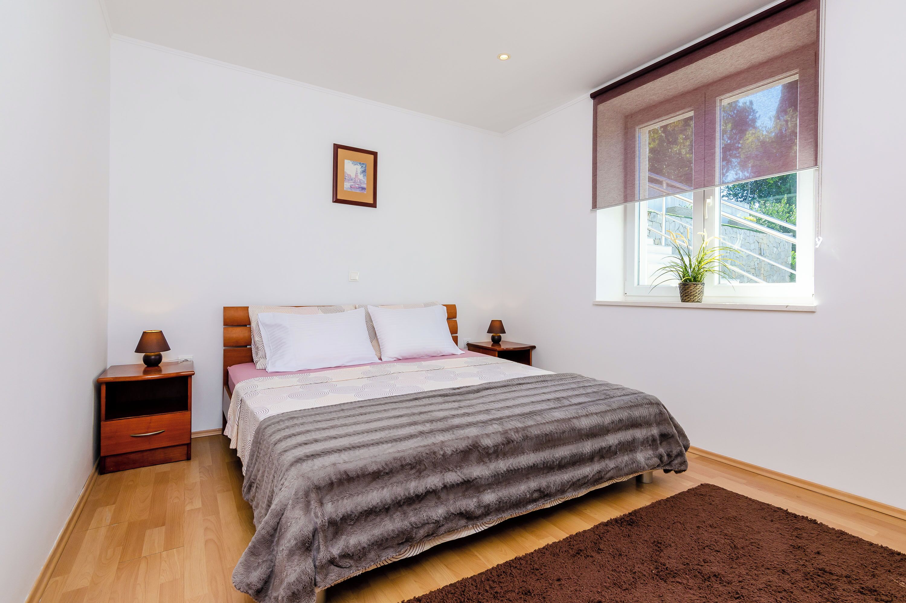 A bedroom with a bed, nightstands, a window with a plant, and a picture on the wall.